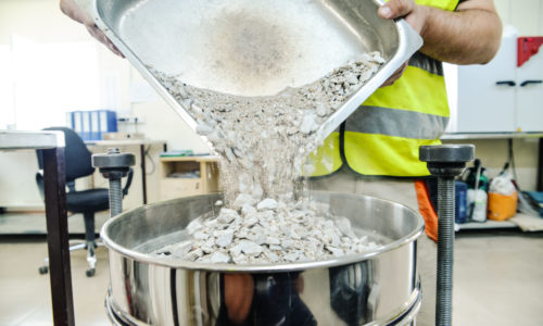 On site road testing laboratory. Placing sample of gravel into a silver container. Preparation step - pouring sample of a layer of soil